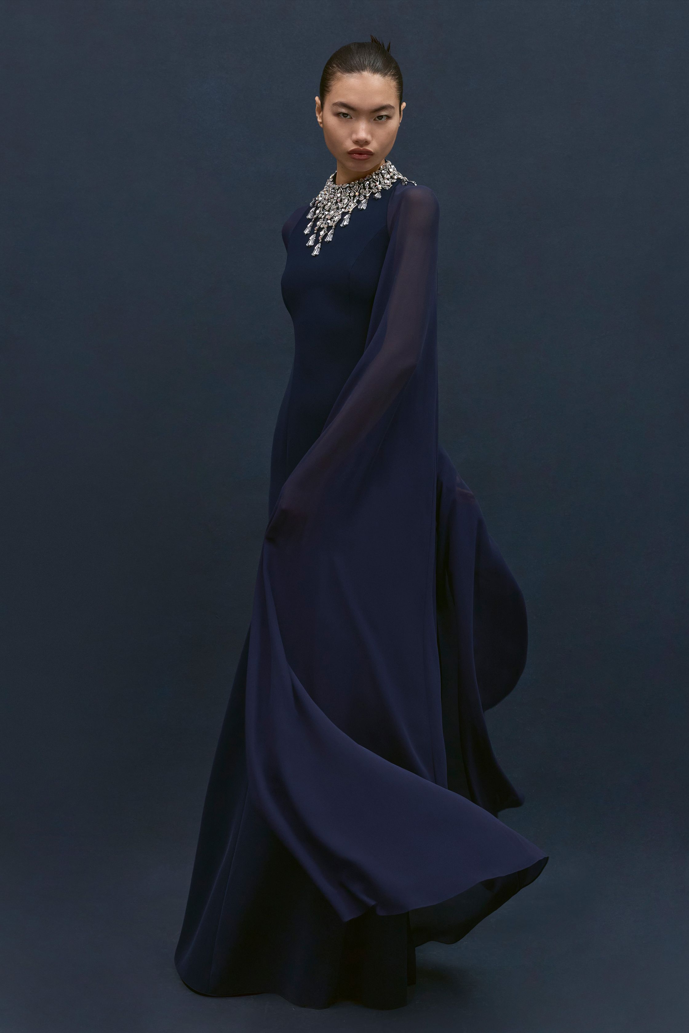 Jenny Packham本季延续品牌标志性的红毯礼服风格，以闪耀流苏、金属光泽与修身长裙构建极具戏剧感的夜晚造型。银色亮片与深蓝礼服形成冷艳优雅的视觉对比，垂坠流苏与贴身剪裁让服装在行走间呈现波光般的流动感。设计在极简轮廓中加入华丽装饰，使整个系列既保留经典好莱坞 glamour，又展现现代女性的自信与优雅-顽石频道趋势研究